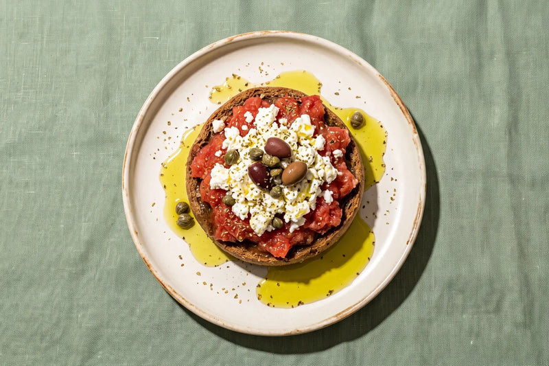 Cretan dakos with grated tomato, mizithra, capers and olives drizzled with extra virgin olive oil