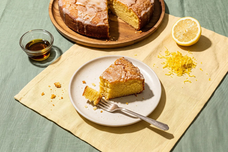 Slice of lemon olive oil cake with lemon zest beside the whole cake