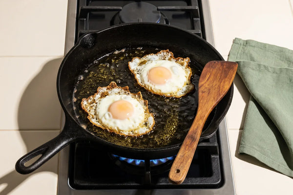 Eggs frying in extra virgin olive oil in a cast-iron skillet on a gas stove