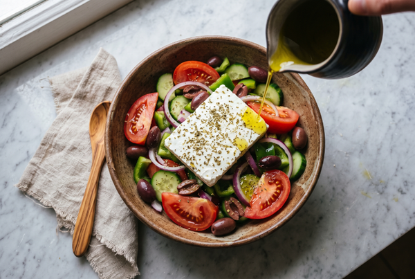 Greek village salad in a rustic bowl with olive oil being poured